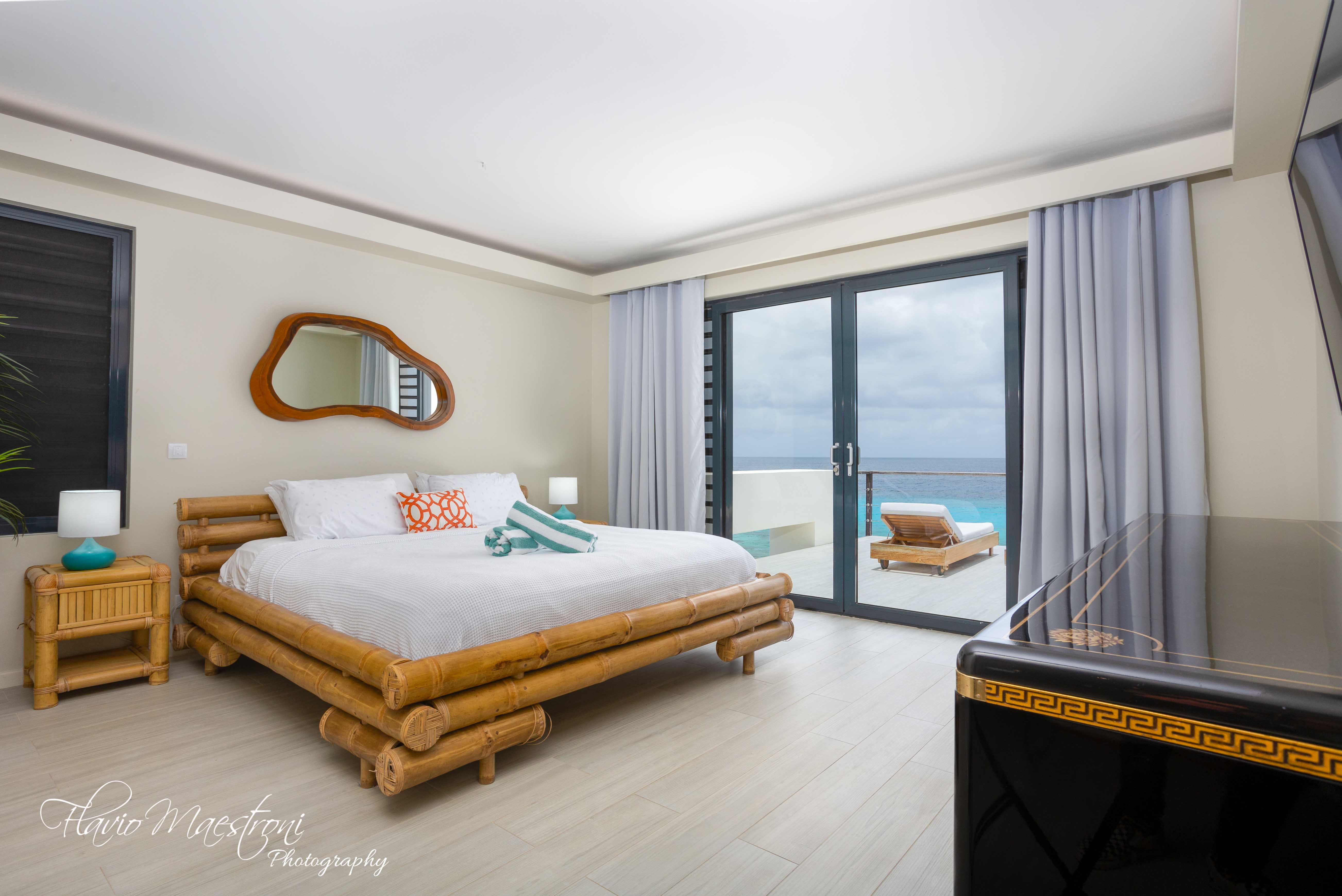 Luxury Bonaire villa master suite with a natural bamboo king bed, private terrace, and stunning ocean views over a private pool.